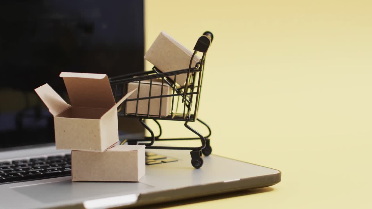 video de portátil con pantalla en blanco, carrito de compras y cajas con espacio de copia sobre fondo amarillo