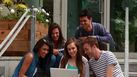 Cheerful-friends-using-laptop-on-stairs