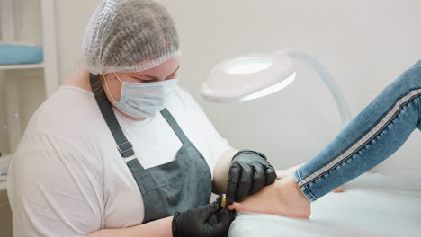 technician in protective gear carefully places pedicure tools on client toe during foot care session in clean, well-lit salon, with client relaxing on treatment bed under white lamp