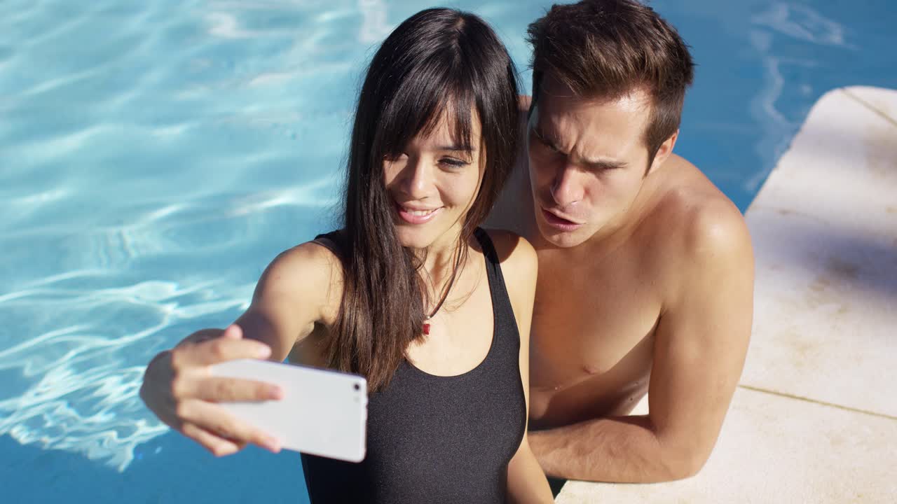 una pareja guapa toma una foto mientras está de pie en la piscina