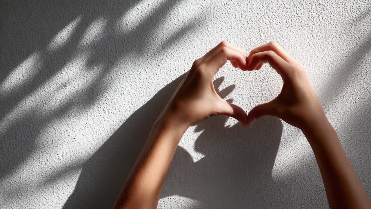 A Beautiful Display of Affection: Forming a Heart Shape with Hands Against a Light-Textured Wall, Capturing Love and Connection Through Subtle Shadows
