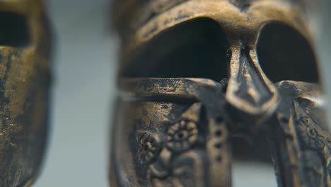 a zoom-in macro shot of a spartan design, two different ancient warrior metal bronze helmets, textured shapes, studio lighting, full hd cinematic video, hyper slow motion 120 fps, pan right