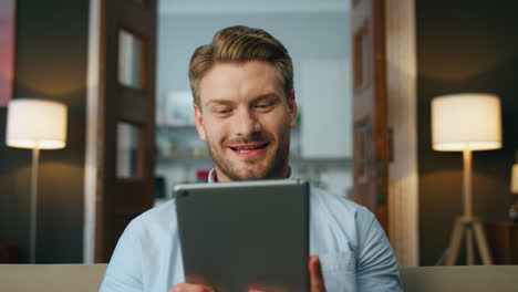 hombre sonriente viendo la pantalla de la tableta sala de la noche. primer plano emocionado hombre logrando