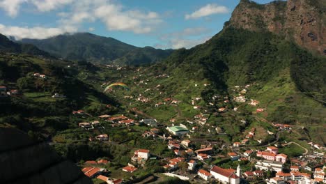 paraglider flies above small village porto da cruz on madeira island, aerial