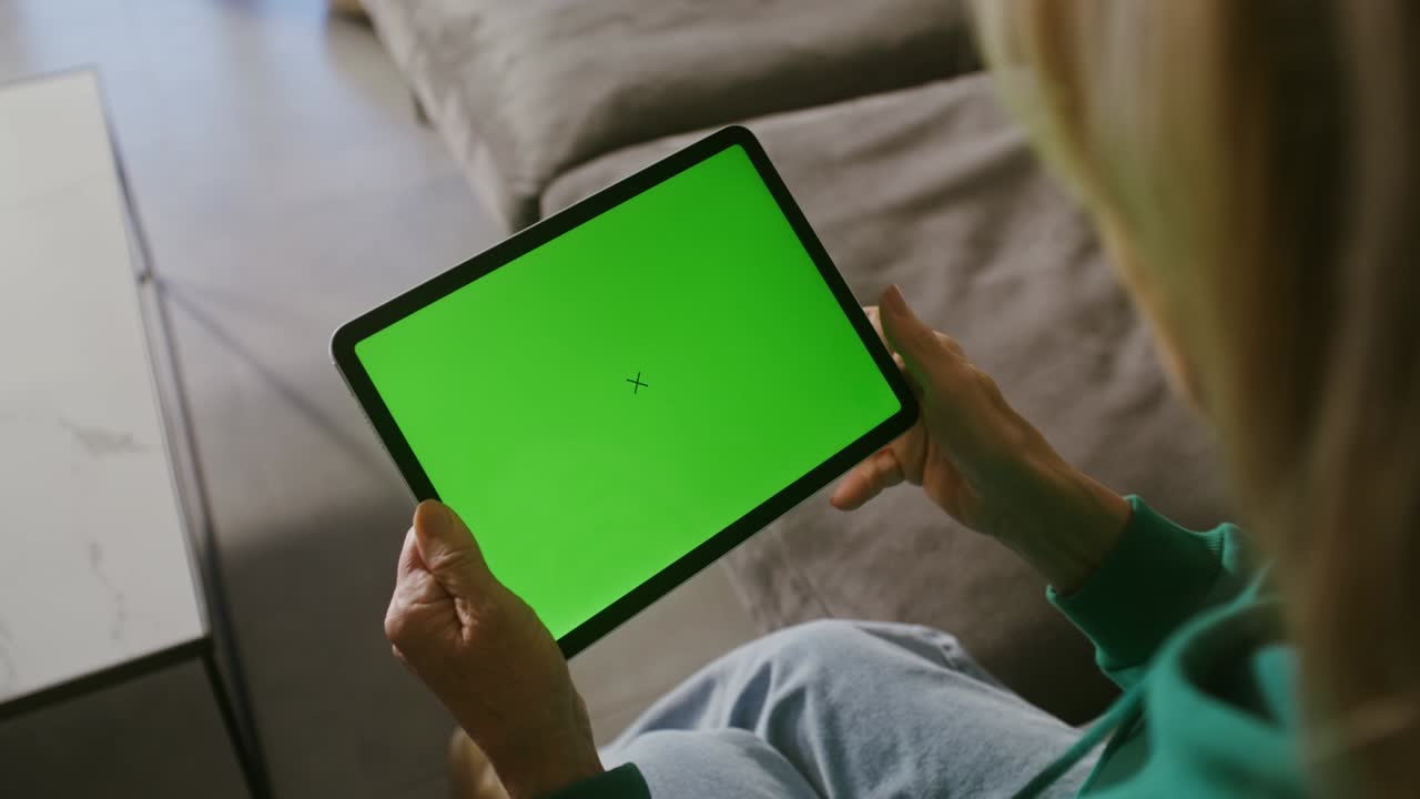 소파에 앉아 있는 태블릿에서 비디오 통화를 시작하는 미소 짓는 노인 여성