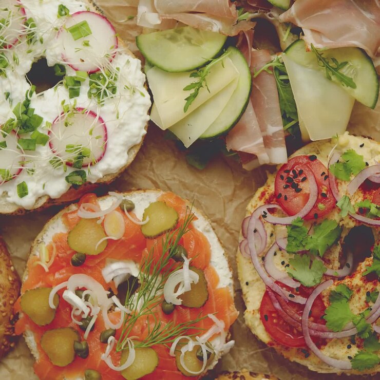 Bagel servito con vari condimenti: salmone, prosciutto, formaggio fresco e hummus.