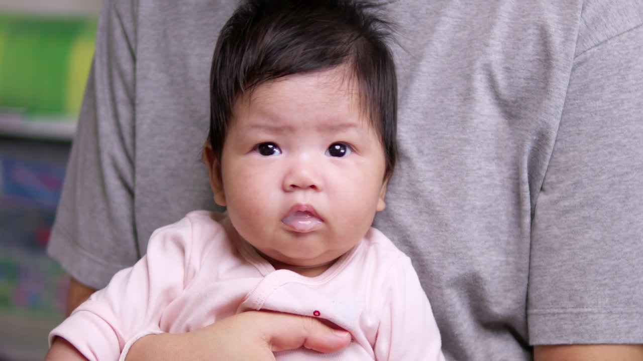 Moving its head from side to side and squirming a little from its mother's grasp, a newborn baby's saliva is coming from its tiny mouth.