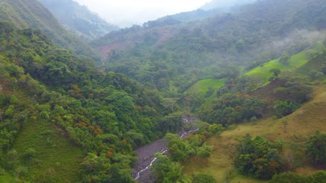 aerial drone shot following a dry river through a valley between mountains surrounded by nature in risaralda, colombia