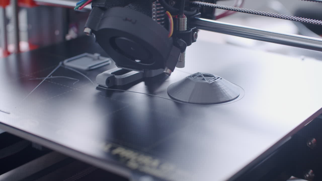 3d printer prints on a heated bed with grey filament. the printing process is almost finished.