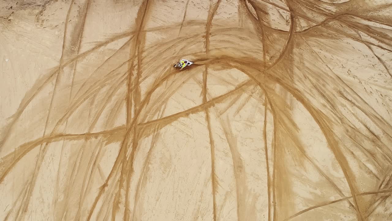 모토크로스 모터사이클 라이더가 모래 언덕을 타고 돌아갑니다. 느린 동작입니다.