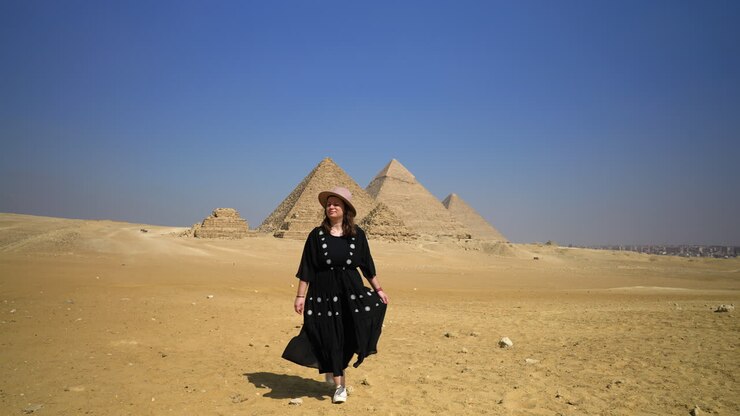 chica vestida de negro caminando en el desierto, pirámides en el fondo en el cairo, egipto - tiro ancho