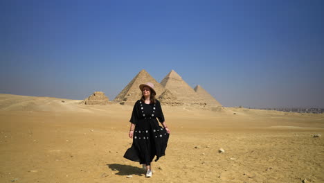 girl in black dress walking in the desert, pyramids in the background in cairo, egypt - wide shot