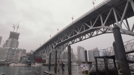 Man-waiting-for-ferry-under-the-Granville-Island-bridge-on-cloudy-day