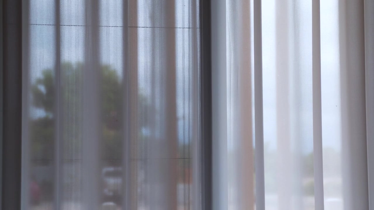Close-up of a sheer white curtain filtering natural daylight through a home window. Minimal interior design creating a bright, airy atmosphere with soft diffused light.