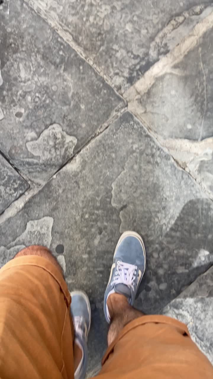Yaz aylarında Avrupa'nın eski bir şehrinde taş bir yol veya kaldırımda yürüyen erkek turist. Şehri keşfetmek ve yürüyerek gezip görmek. Ayakların ve ayakkabıların yukarıdan aşağıya doğru çekilmiş görüntüsü. Tatilde eski mekanları ziyaret etmek
