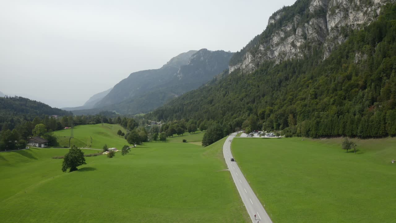 Long stretch of road running through lush green valley framed by towering cliffs and forested slopes.