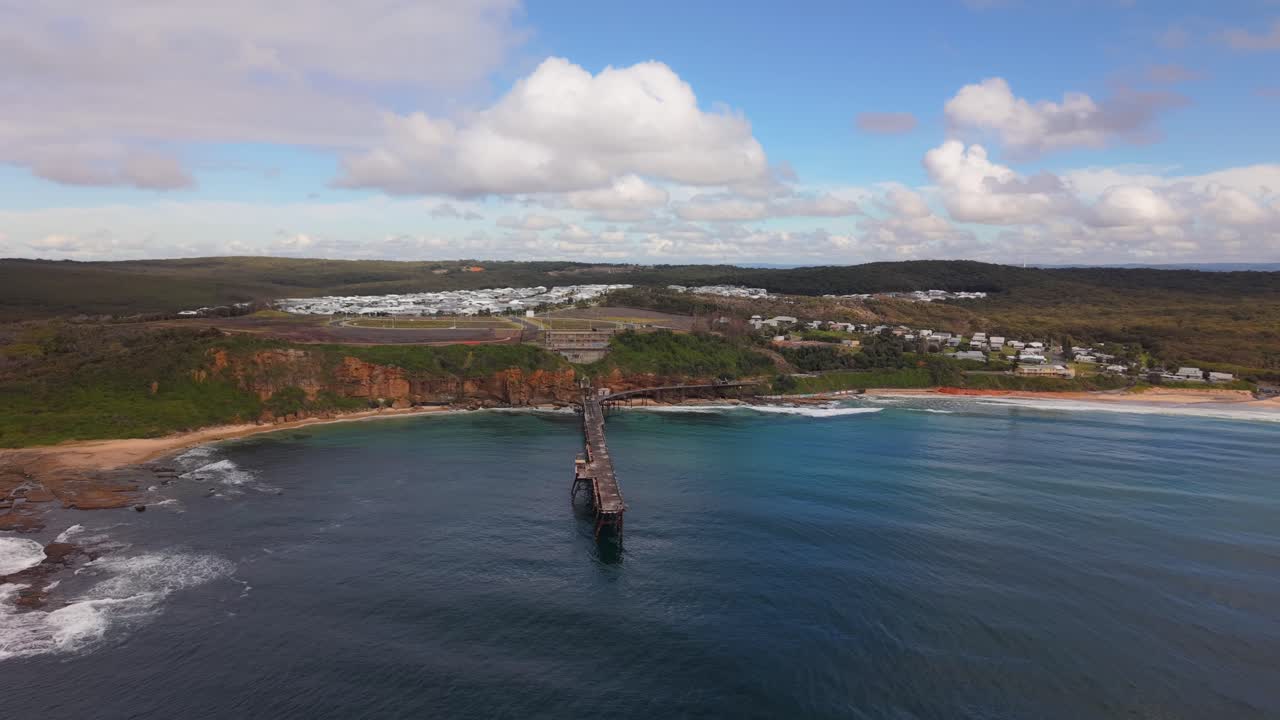 Wide aerial of Catherine Hill Bay ocean waters and jetty stretching out in New South Wales, orbit approach