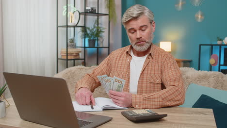 mature man sitting on sofa table with laptop and calculator managing family budget at home