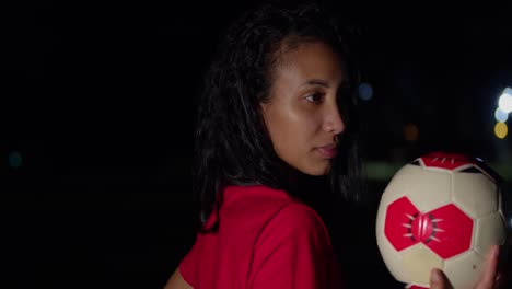 With-a-football-in-her-hand,-a-young-girl-in-a-bikini-stands-under-the-night-sky