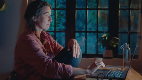 tired woman rubbing eyes and working on laptop in the evening at home