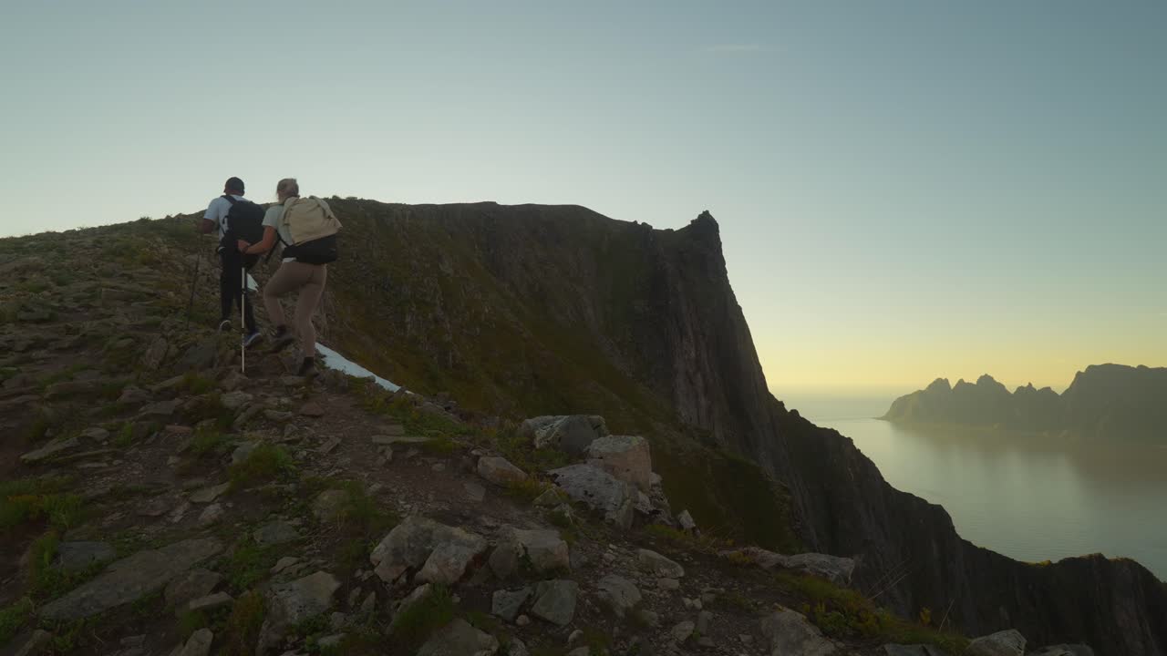 una pareja joven subiendo una montaña en senja, noruega durante el amanecer
