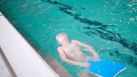 boy is practicing backwards swimming inside huge pool with swim board