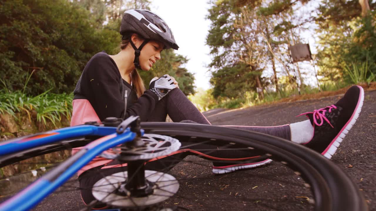 Ciclista di mountain bike donna seduta a terra con dolore