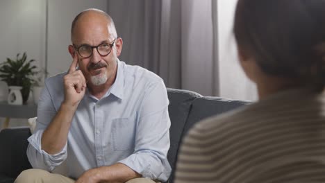 mature man sitting on sofa talking with female counsellor about general or mental health issue 12