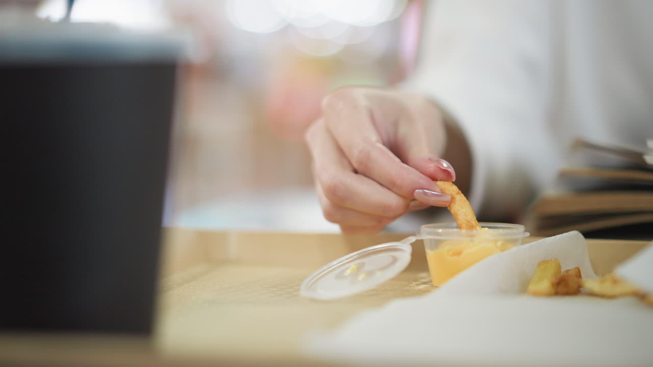 primer plano de la mano recogiendo patatas fritas crujientes con un recipiente de salsa de queso en el lado, colocado en una bandeja en una configuración de comedor casual, una bebida también es visible, mejorando la experiencia de la comida