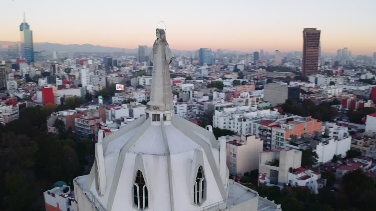 amplias tomas de drones de la enorme estatua de jesús en la parroquia del purismo corazon de maria, con la ciudad de méxico al atardecer y un parque con muchos árboles al fondo