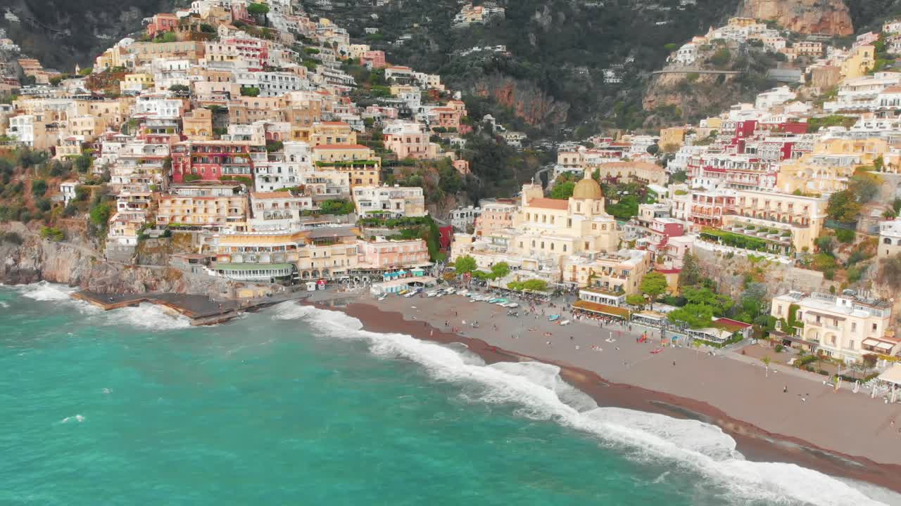 Aerial view of Positano, Italy on a stormy day. The town is nestled on a cliff overlooking the Mediterranean Sea. The colorful houses and buildings on the hills are silhouetted against the dark clouds