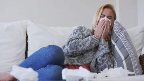 sick woman with tissue sneezing while lying on couch at home