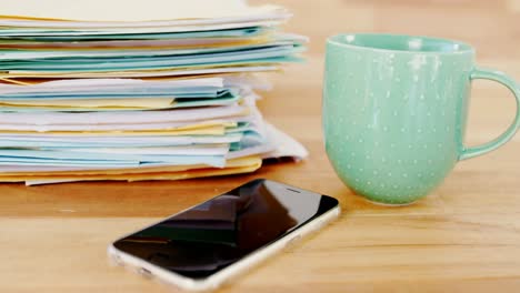 taza de café, teléfono móvil y archivos apilados en la mesa