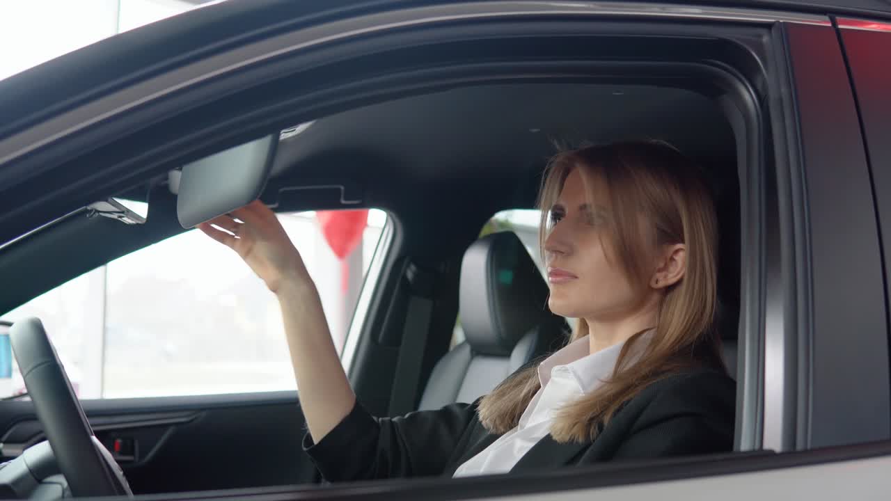 Beautiful woman looks in the mirror in the car at a car dealership