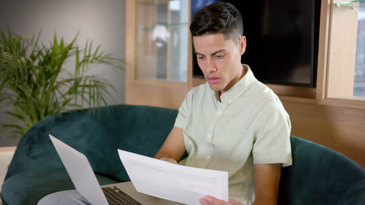 Reviewing documents, man working on laptop while sitting on couch