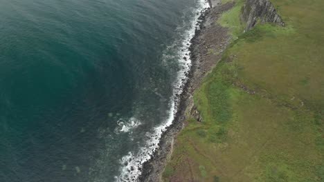 drone shot of sea cliff in the coast of isle of skye scotland, clear blue water and green grass