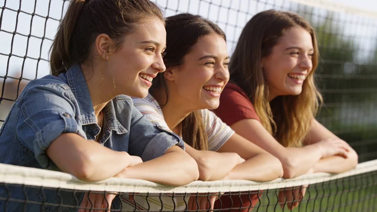 Adolescenti sorridenti appoggiati alla rete da tennis in campo, con capi in denim a righe bordeaux, rispondendo a una chiamata fuori campo