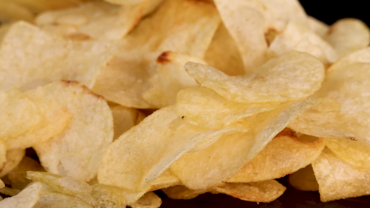 A hand zooms in and grabs potato chips from a pile under dramatic studio lighting