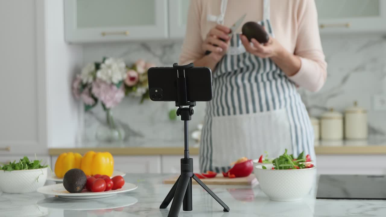 Donna con grembiule registra un vlog di cucina sul cellulare.