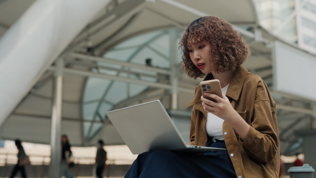Young woman working on laptop and smartphone outdoors