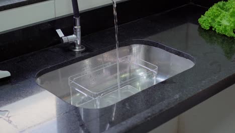 a black sink with water running inside a pot for washing fresh lettuce