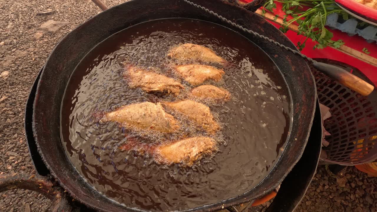 Panerede fiskefileter steger i varm olie og bliver gyldenbrune med boblende skorpe. Klassisk gade-fisketilberedning udendørs, der viser sprød belægning dannes i en aktiv stegeproces.