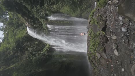 man walks in misty river to base of tiu kelep waterfall in lombok, idn