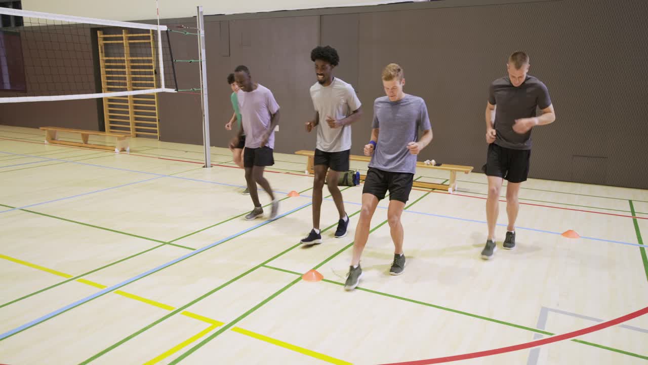 Diverse male teammates on cue performing footwork drill in gym over court lines near cones