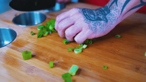 Cebollas-Picadas-Arrojadas-Por-Una-Mano-Tatuada-Sobre-Una-Tabla-De-Cortar-Del-Chef