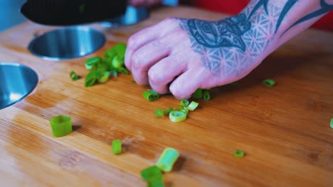 cebollas picadas siendo arrojadas por una mano tatuada en una tabla de corte de chefs