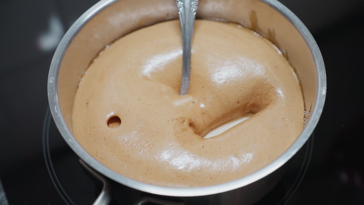 primer plano de la sustancia blanca dentro del pap hinchado con una cuchara sumergida en la olla, textura gruesa y burbujeante que se forma en la superficie a medida que se cocina en la estufa, mostrando consistencia cremosa y color rico