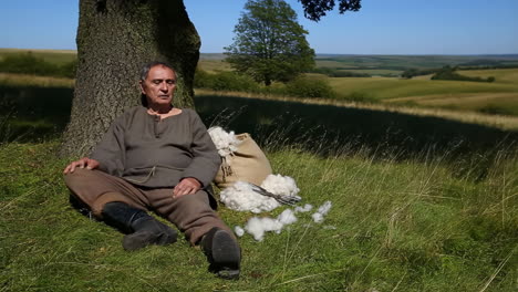 a man sitting under a tree with wool and shears in a rural landscape