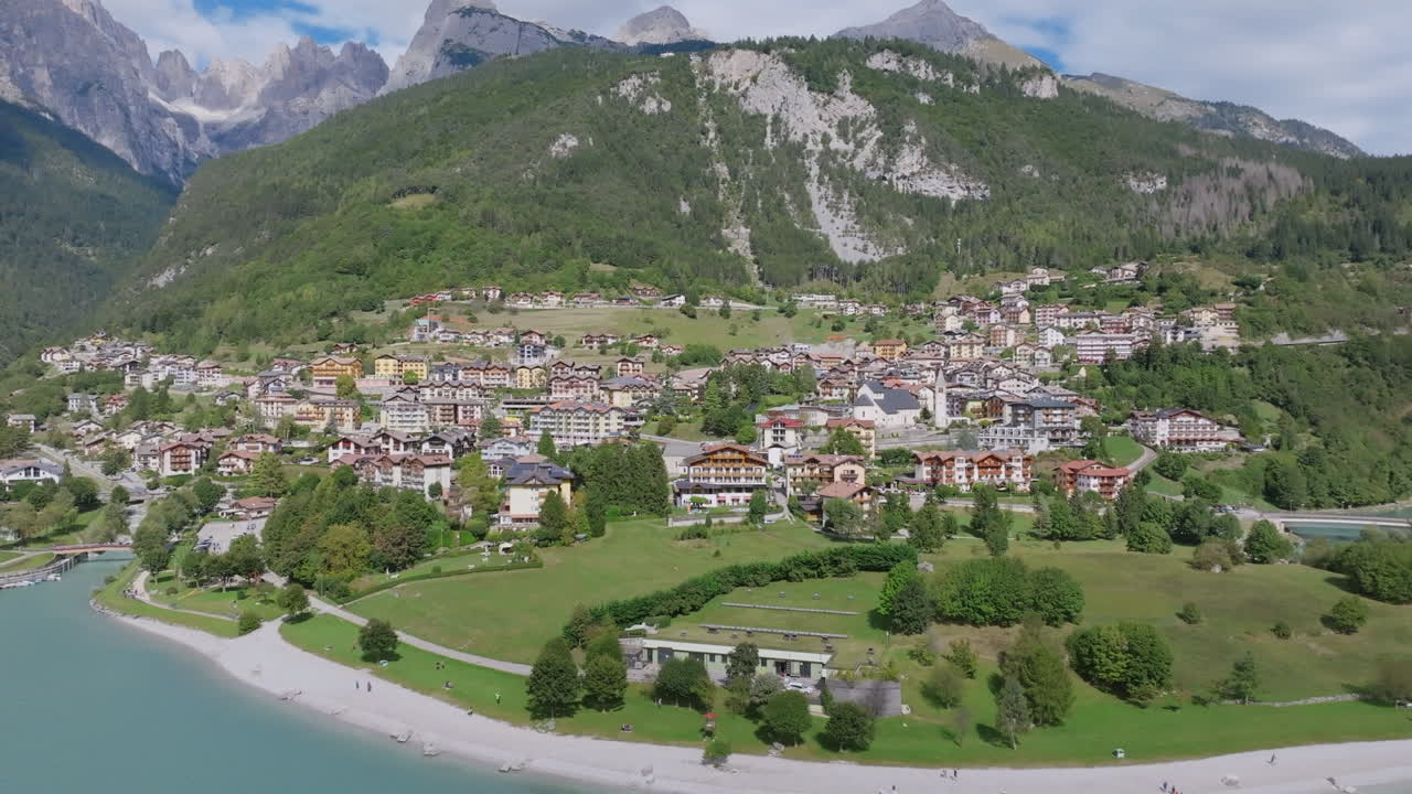 Wide aerial video moving away from the town of Molveno in northern Italy with the Dolomite mountains in the background.
