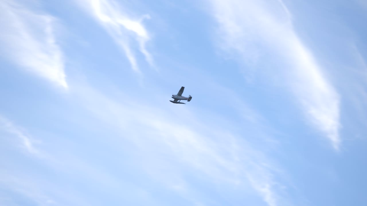Floatplane flies overhead against a blue sky filled with cirrus clouds.